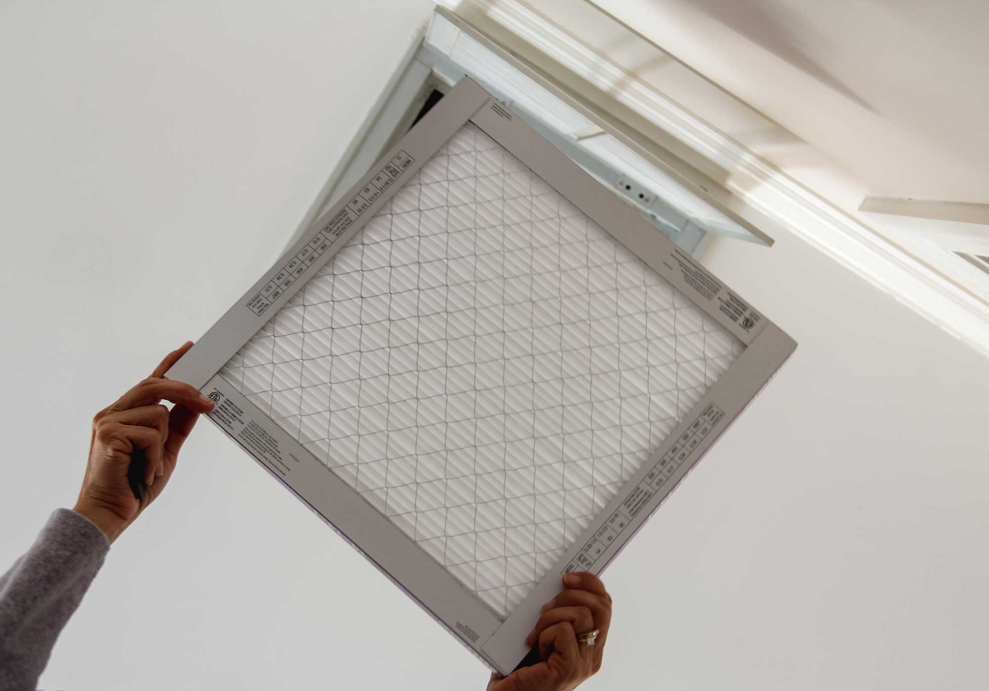 Homeowner replacing a residential air conditioning filter to avoid costly air conditioning repair service calls.