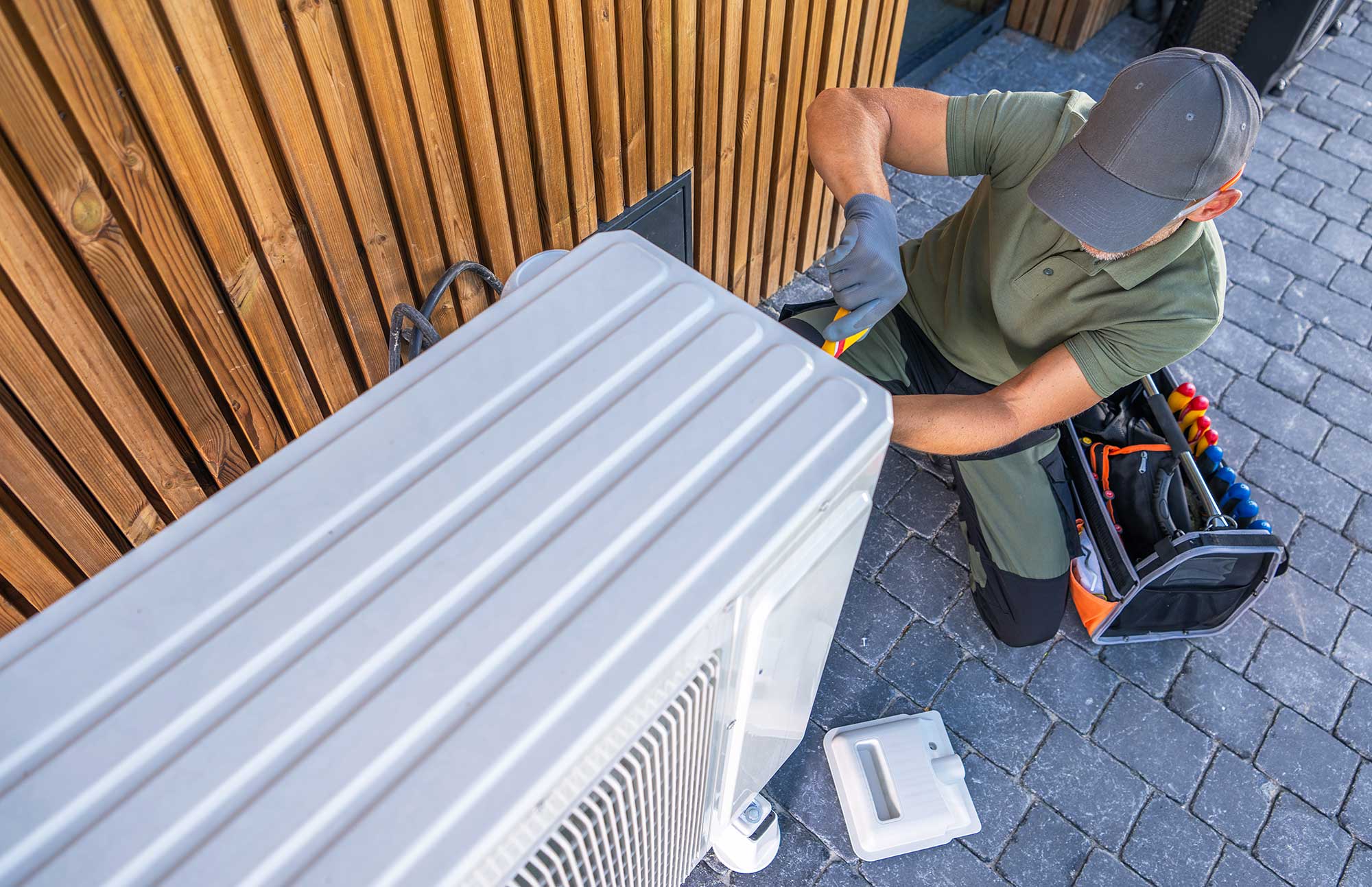 An HVAC company technician repairing an outdoor AC unit for a homeowner.